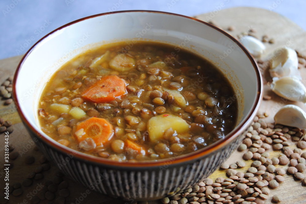 Vegan Lentil Soup with Vegetables served in brown bowl, on wooden kitchen board. Close up view. Vegan Lentil Soup with Vegetables served in brown bowl, on wooden kitchen board. Close up view.
