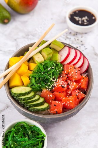 Salmon poke with avocado, salmon, cucumber, radish and rice) on dark background , top view. Asian trendy food
