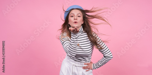 Young cute caucasian lady with flying hair in a fashionable beret on a pink background.