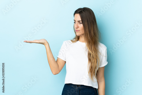 Young caucasian woman over isolated background holding copyspace with doubts