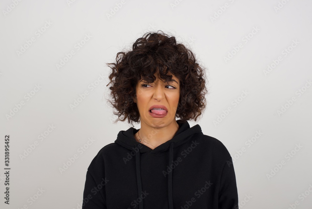 Body language. Disgusted stressed out pretty girl posing against gray wall, frowning her face, demonstrating aversion to something. Body language. Disgusted stressed out pretty girl posing against gray wall, frowning her face, demonstrating aversion to something.