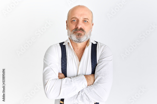 Mature people, age and retirement concept. Serious Caucasian retired businessman wearing white shirt and suspenders looking at camera with confident facial expression, crossing arms on his chest © Anatoliy Karlyuk
