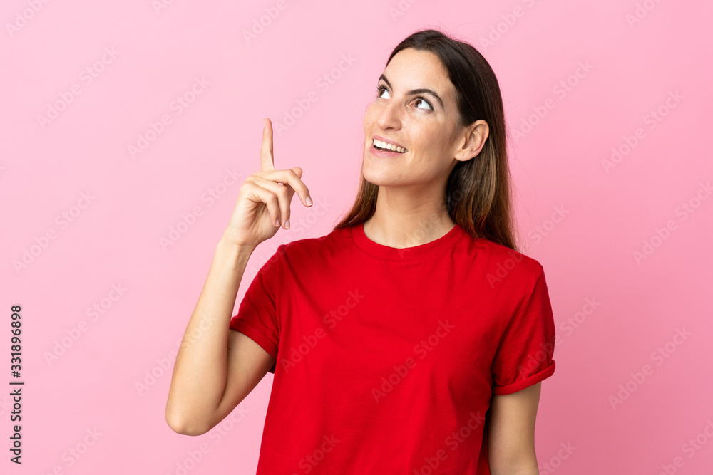Young caucasian woman isolated on pink background pointing up and surprised