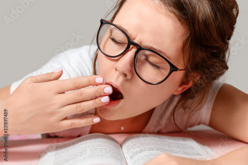 A young woman with glasses yawns. Read books.