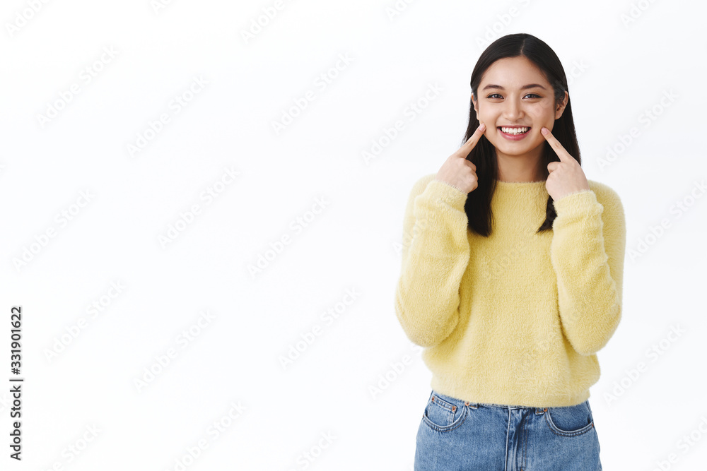 Kawaii asian girl with short dark hair, in yellow sweater, pointing at dimples or cheeks and smiling, showing perfect no blemishes skin, promote korean makeup, cosmetology products, white background Kawaii asian girl with short dark hair, in yellow sweater, pointing at dimples or cheeks and smiling, showing perfect no blemishes skin, promote korean makeup, cosmetology products, white background