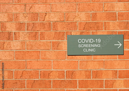 a COVID-19 Screening Clinic sign on a red brick wall © Kim Britten