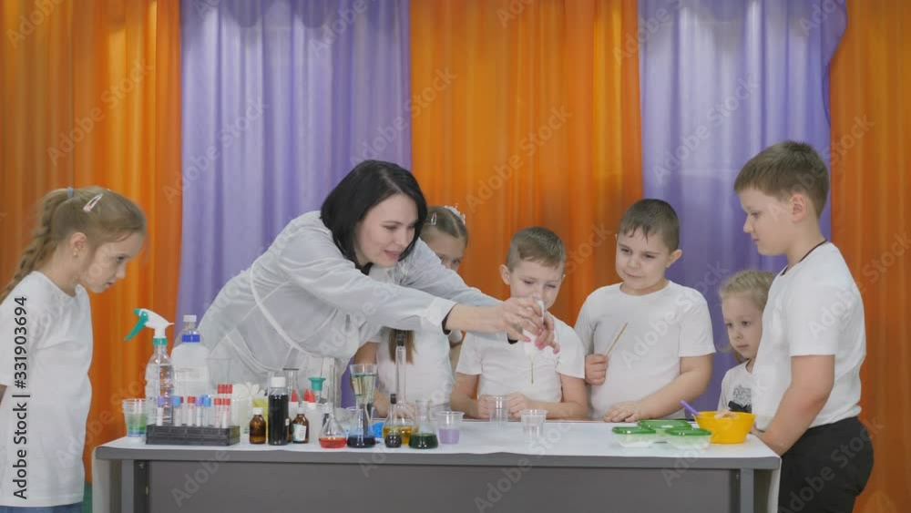 Chemical experiments for children. Woman pours a green substance into a clear glass. Children are surprised. The boy takes a long green worm out of the liquid. Room is filled with artificial smoke. Chemical experiments for children. Woman pours a green substance into a clear glass. Children are surprised. The boy takes a long green worm out of the liquid. Room is filled with artificial smoke.