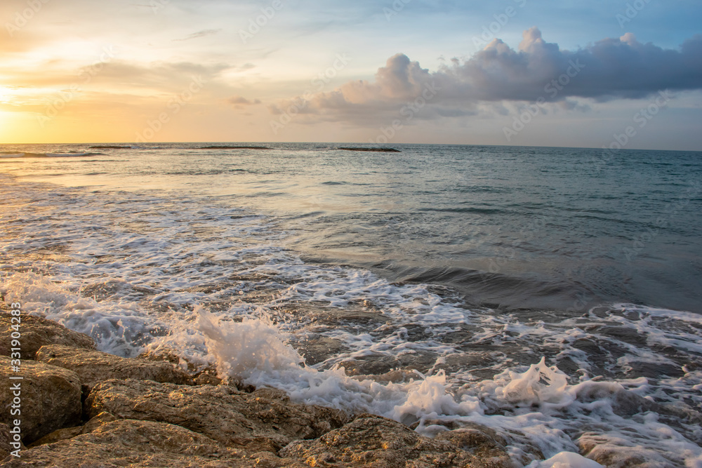 Sunshine from horizon on the stones of the seashore with waves and white bubbles during the summer time in Bali Sunshine from horizon on the stones of the seashore with waves and white bubbles during the summer time in Bali