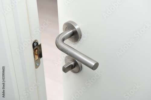 Detail of a metallic knob on white door horizontal.Stainless steel handle on a white wooden door.The door is open.