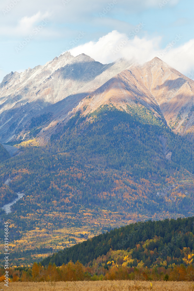 Beautiful rocky mountains and yellowed forest in a foothill valley on an autumn day. Natural background, mountain landscape. Russia, Siberia, Buryatia, Eastern Sayans, Baikal region