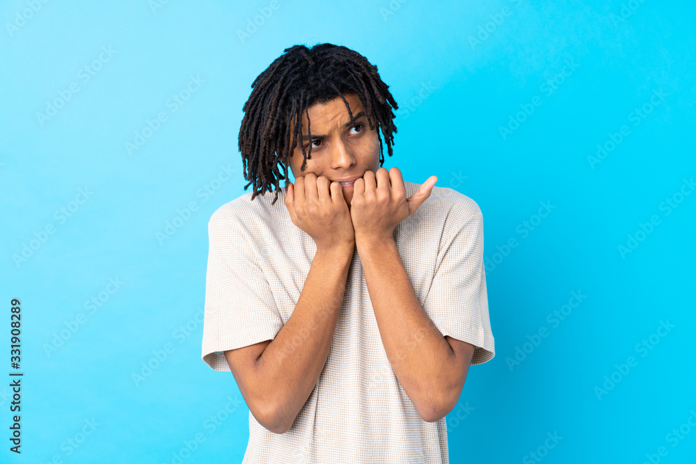 Young African American man over isolated blue background nervous and scared putting hands to mouth Young African American man over isolated blue background nervous and scared putting hands to mouth
