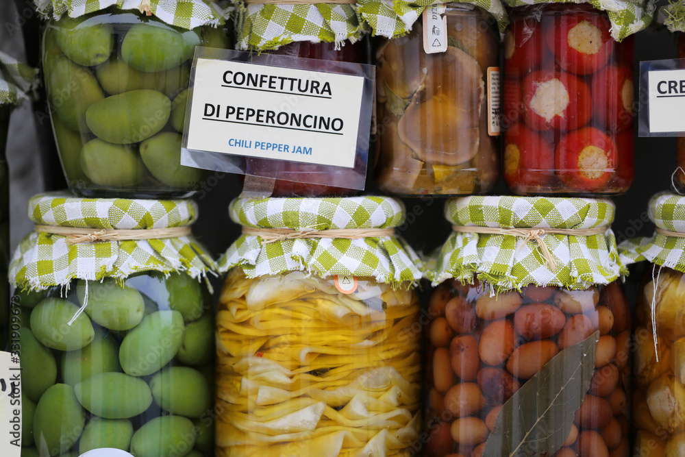 Glass jars of pickled preserved vegetables including chilli peppers, onions., olives. Puglia, Italy Variety of vegetables pickled in jars