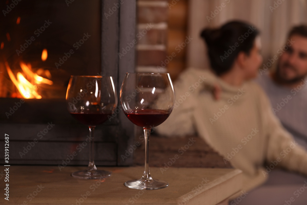 Lovely couple near fireplace at home, focus on glasses with wine. Winter vacation