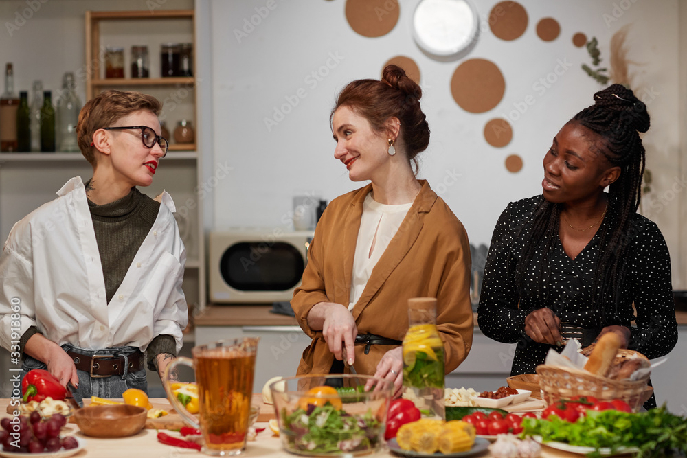 Group of young beautiful women standing in the kitchen cutting vegetables for salad and talking during cooking