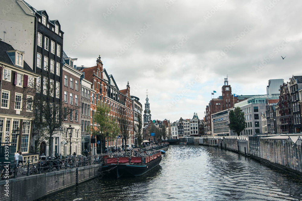Filtered cityscape of Amsterdam. Dutch city architecture. Modern exterior of buildings. Boat in canal. Tourism in Europe.