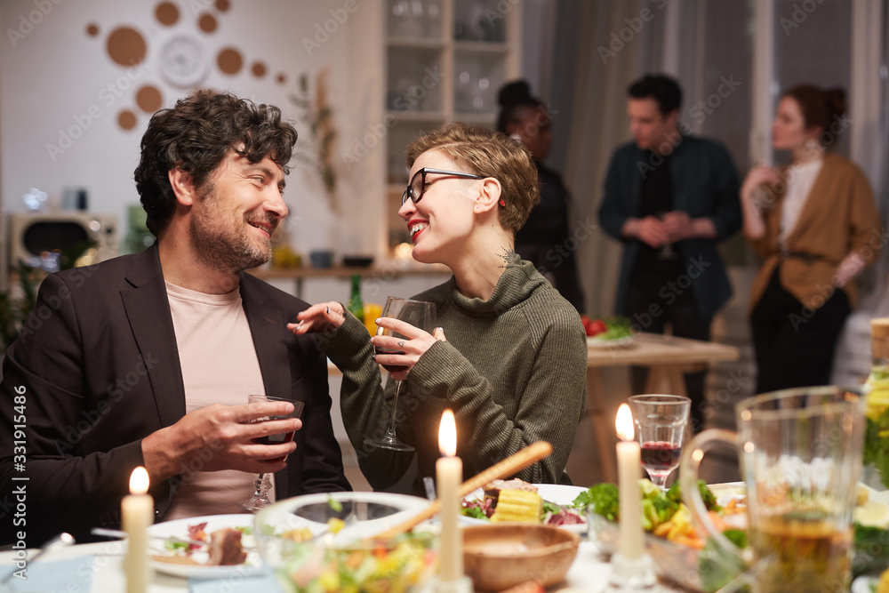 Young happy couple sitting at the holiday table with wine glasses and talking during party at home Young happy couple sitting at the holiday table with wine glasses and talking during party at home
