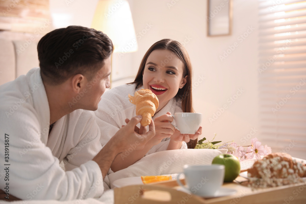 Happy couple in bathrobes having breakfast on bed at home Happy couple in bathrobes having breakfast on bed at home