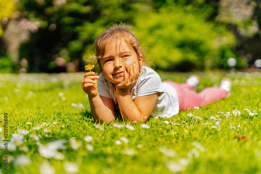 Young Caucasian white girl holding yellow Buttercup flower on meadow, lying on field with many yellow buttercups and white daisies flowers, summer day Young Caucasian white girl holding yellow Buttercup flower on meadow, lying on field with many yellow buttercups and white daisies flowers, summer day