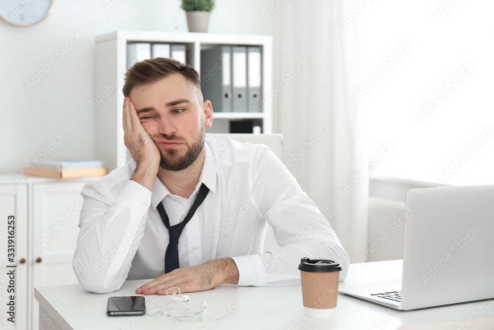 Lazy young man wasting time at table in office Lazy young man wasting time at table in office