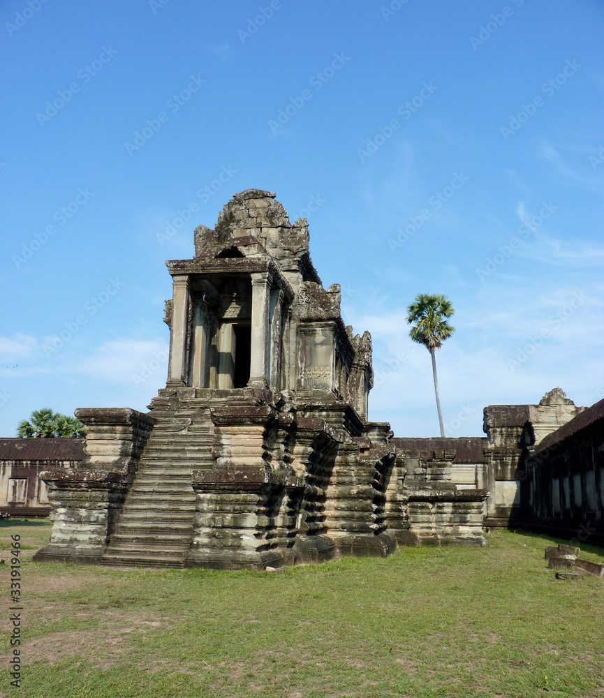 Naklejka premium Stone library building of Angkor Wat on green grass before blue sky, ruins of Angkor, Cambodia