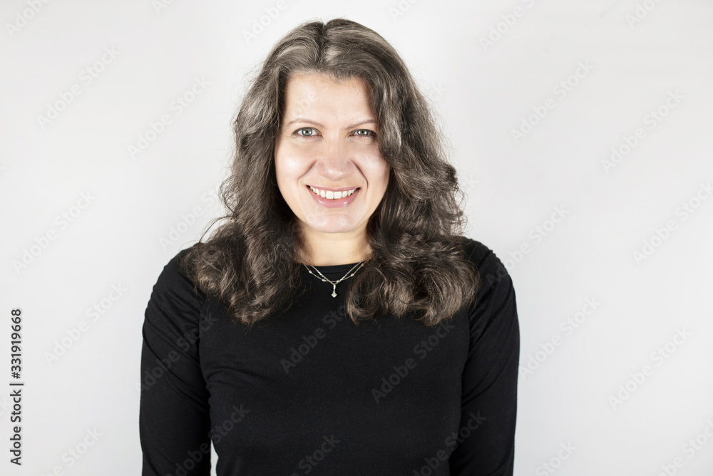 Beautiful middle-aged woman on light background with dark hair starting to turn gray. The woman is happy and smiling because she goes to the hairdresser Beautiful middle-aged woman on light background with dark hair starting to turn gray. The woman is happy and smiling because she goes to the hairdresser