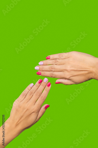 Closeup view vertical photography of two beautiful manicured female hands isolated on green background. Woman showing her fresh stylish professional asymmetric colourful naildesign of fingernails.