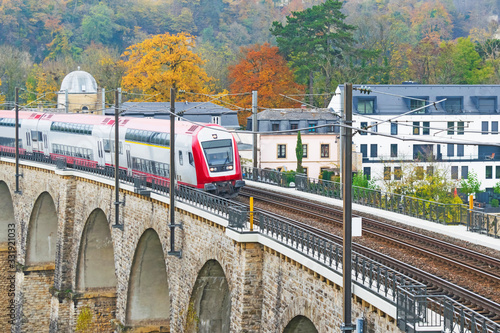 Detail of electrical railroad in Luxembourg city with train, rails, contact lines and viaduct structures in dark autumn day illustrating urban transport concept, Luxembourg.