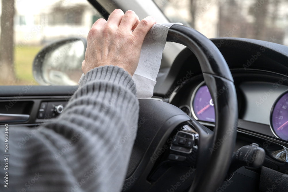 Man cleaning steering wheel of a car using antivirus antibacterial wet wipe (napkin) for protect himself from bacteria and virus.