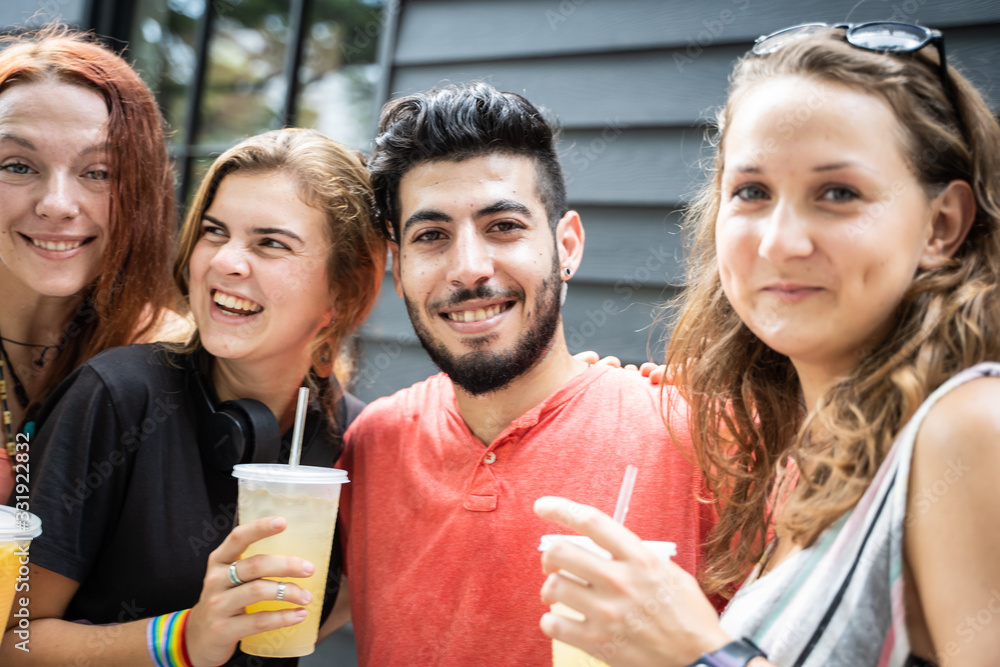Obraz premium People from different ethnic groups smiling with a juice in a plastic container in their hands and with bracelets with the lgtb flag