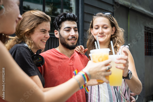Group of four young people of different ethnicities toasting with juice in a plastic cup