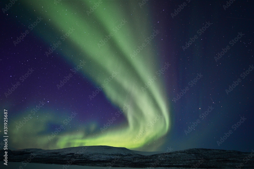 dancing green northern lights in the night sky over a mountain range in lapland finland