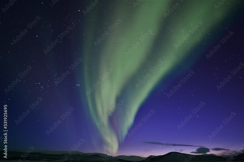 dancing green northern lights in the night sky over a mountain range in lapland finland