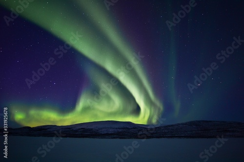 dancing green northern lights in the night sky over a mountain range in lapland finland