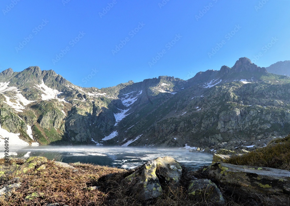 Swiss mountain landscape on a beautiful day with blue sky and white clouds in the foreground a mountain lake with a light fog