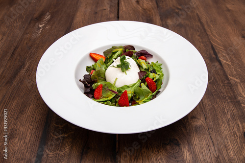 Fresh Italian buratta cheese with mixed salad leaves and strawberry in a plate on a wooden table. Italian cuisine.