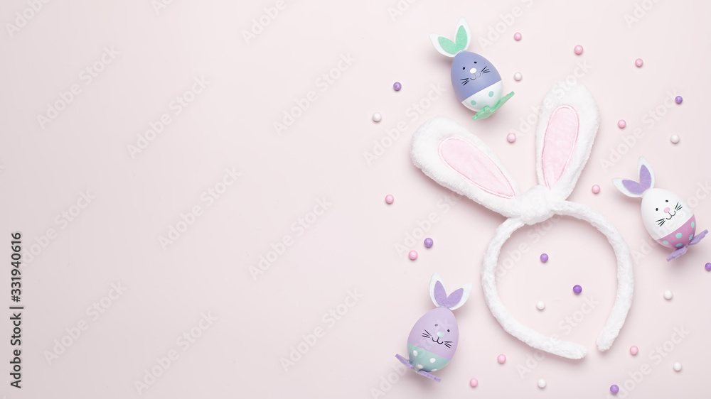 Funny kawaii cute bunny eggs and bunny rabbit ears for kids in pastel colors on pink table top, Easter holiday concept. Easter decoration for kids still life, copy space