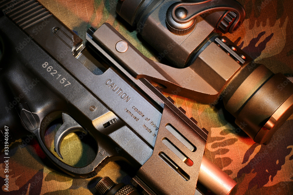 Obraz premium Detalhes de pistola de airsoft com mira acoplada no trilho em fundo camuflado