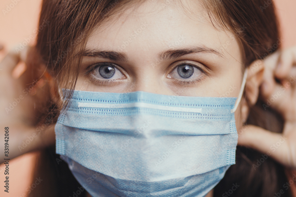 Portrait of young woman putting medical flu mask on face, on colored studio background, quarantine measures and life saving concept Portrait of young woman putting medical flu mask on face, on colored studio background, quarantine measures and life saving concept
