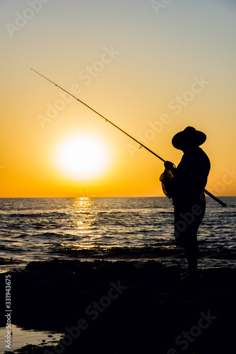 Fisherman prepares to fish at sea. Silhouette of a fisherman fishing at sunset