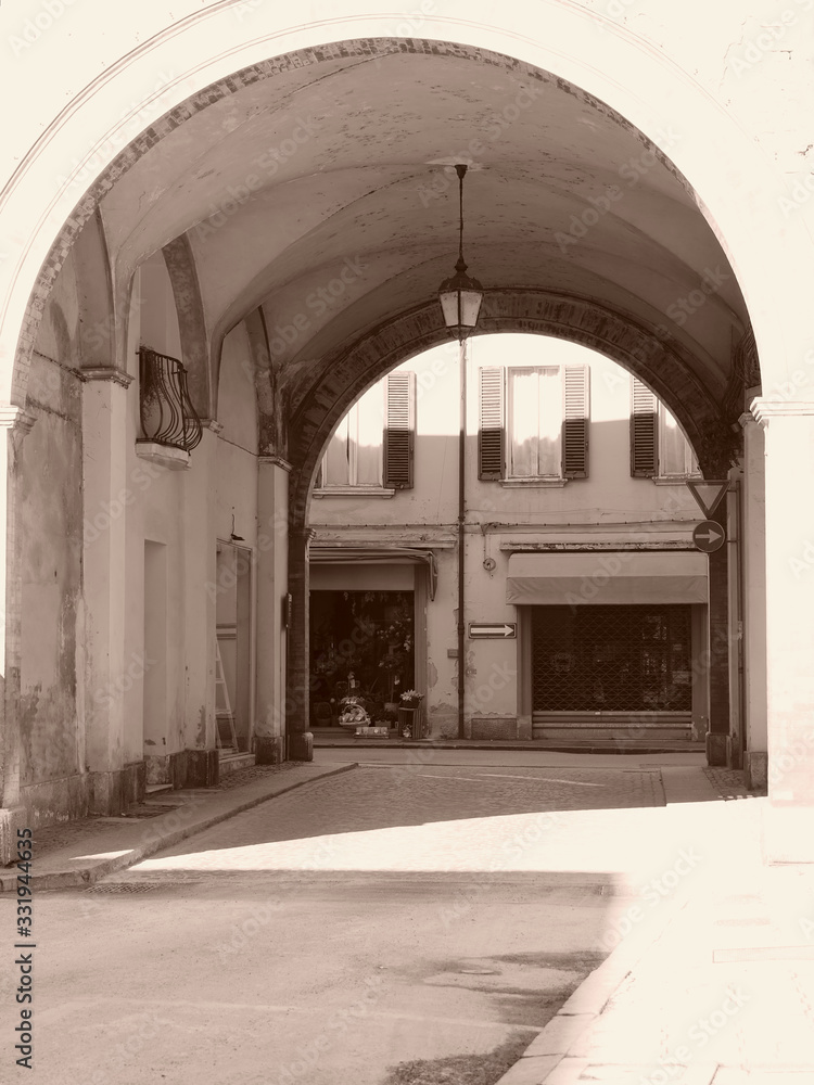 Ferrara, Italy. Downtown, archway and shops. Sunny day. Sepia photo.