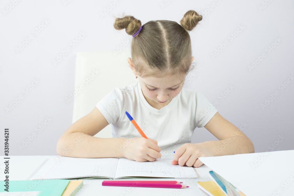 little girl of primary school at the table writes in notebooks and learns lessons, the concept of education little girl of primary school at the table writes in notebooks and learns lessons, the concept of education