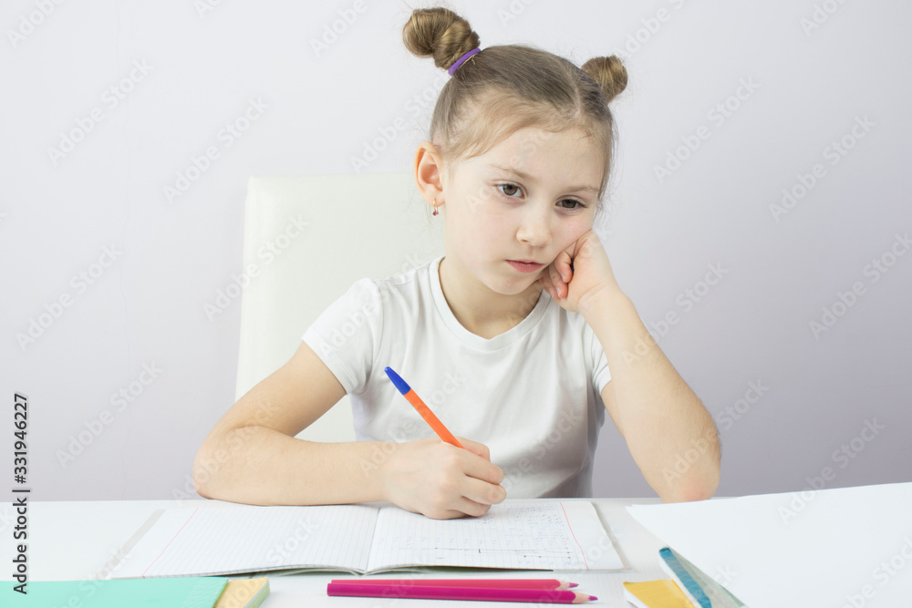 tired and thoughtful little girl of primary school at the table learning lessons, the concept of education tired and thoughtful little girl of primary school at the table learning lessons, the concept of education