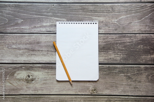 Notepad with a blank white sheet in a checker paper with simple graphite pencil lies on the background of wooden boards.