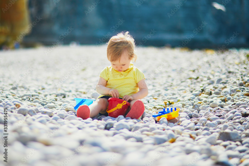 Fototapeta premium Adorable toddler girl playing with pebbles on the beach