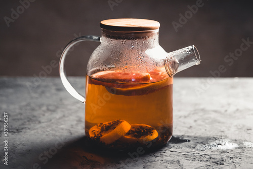 Citrus tea in a transparent teapot. On a gray stone texture background. Healthy drink