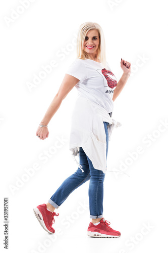 Joyful energetic middle age healthy woman in casual clothes walking and turning at camera. Full body isolated on white background. 
