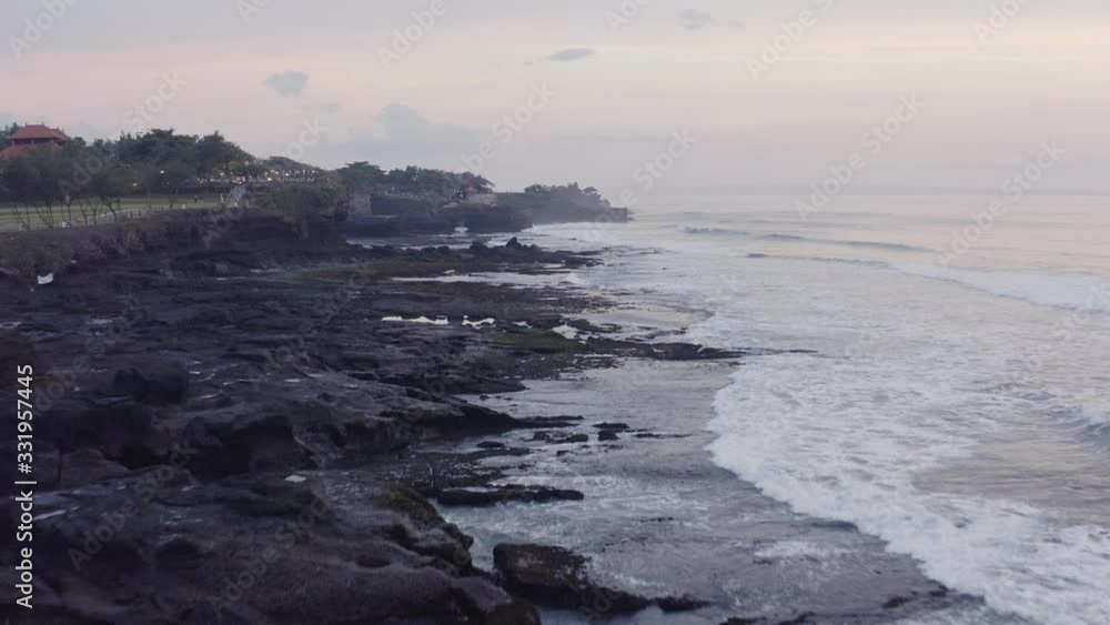 Fly over rocky coast line with huge tidal waves crushing ashore during low tide on the sunset. Tanah Lot, Bali, Indonesia. Fly over rocky coast line with huge tidal waves crushing ashore during low tide on the sunset. Tanah Lot, Bali, Indonesia.