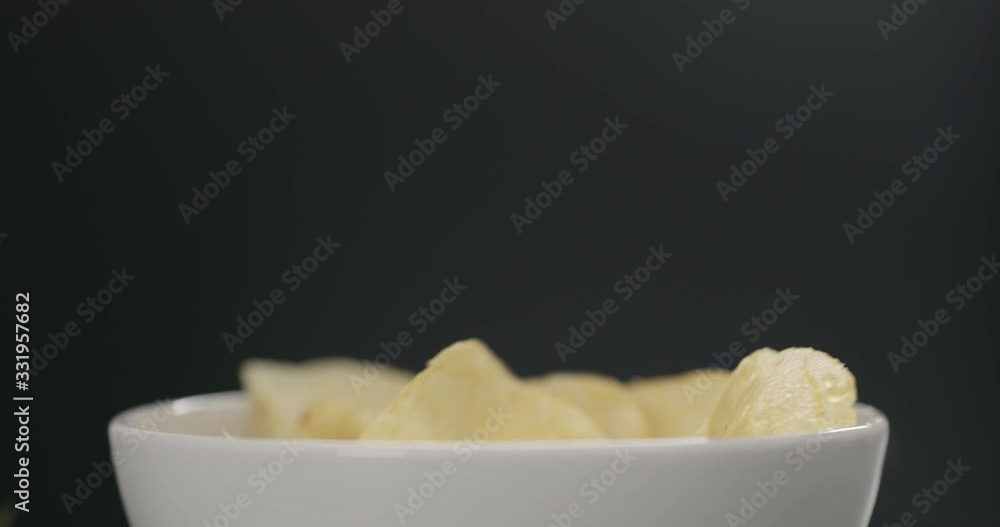 Slow motion potato chips falling into white bowl on black background closeup Slow motion potato chips falling into white bowl on black background closeup