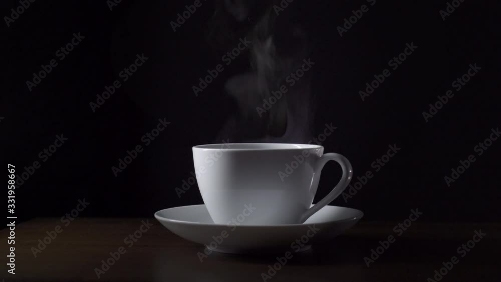 Steam rises from a cup of hot coffee. Black background Steam rises from a cup of hot coffee. Black background