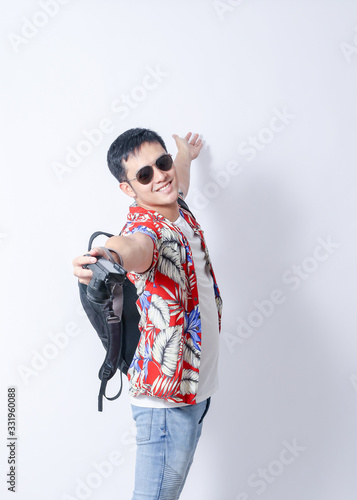 A Portrait of young tourist asian man wearing floral shirt and showing gesture sign. or laptop, Smartphone, camera  and wallet stand in isolated background
